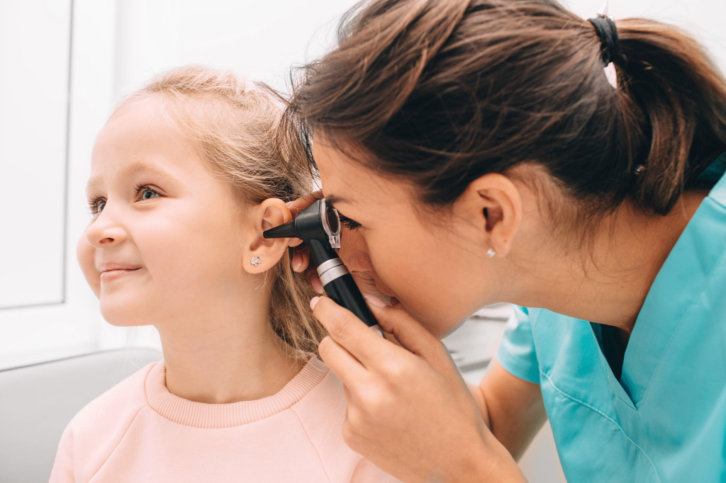Smiling little girl having ear exam with otoscope